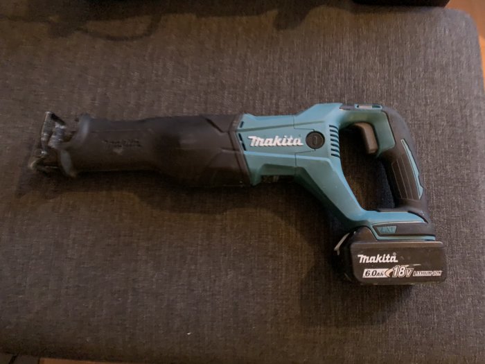 Makita tigersåg med 6,0Ah 18V batteri liggande på en soffa.