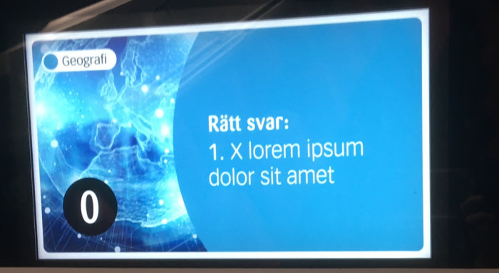 Bildskärm i kollektivtrafik visar quiz med svar "X lorem ipsum dolor sit amet" under kategorin Geografi.