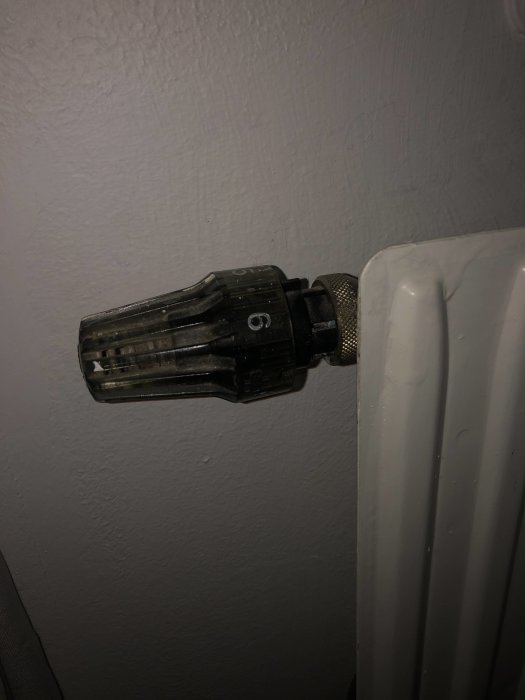 Termostatventil på radiator med guldig justeringsring och begränsat utrymme bakom.