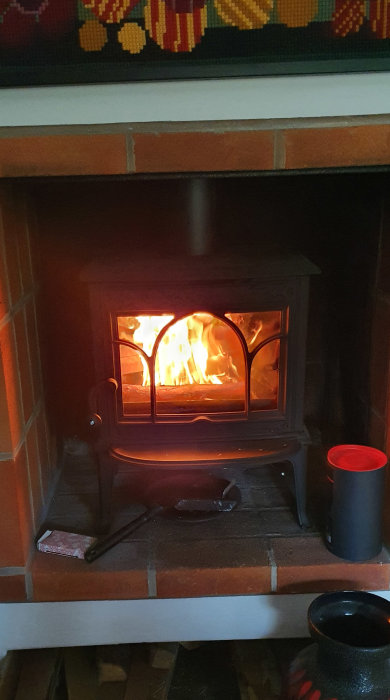 Eld brinner i en gammal Jötul-kamin med öppna luckor, placerad i ett litet rum.