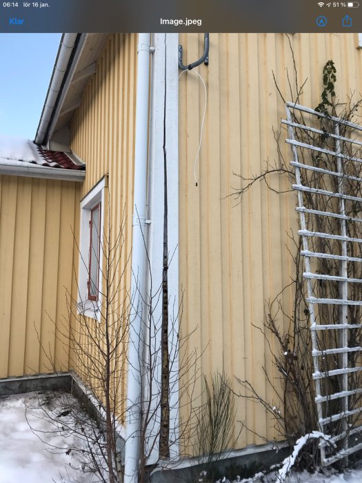 Gult trähus med vit hängränna och gammal elinstallation på utsidan, snö på marken.