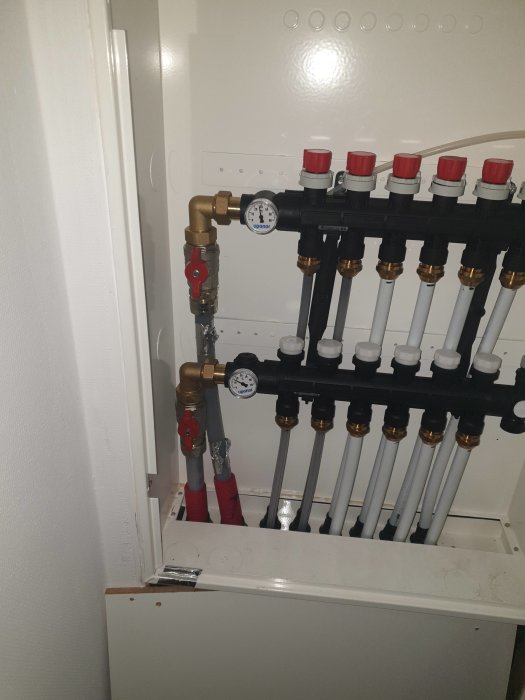 Värmesystem med cirkulationspump, manifold och termostatventiler i teknikskåp.