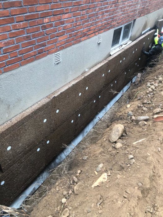 Dräneringsarbeten vid husgrund med isoleringsmaterial och dräneringsplattor synliga.