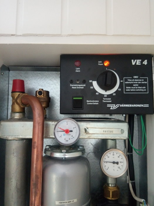 Värmesystem med automatisk avluftare, tryckmätare och kontrollpanel under vit kökslucka.