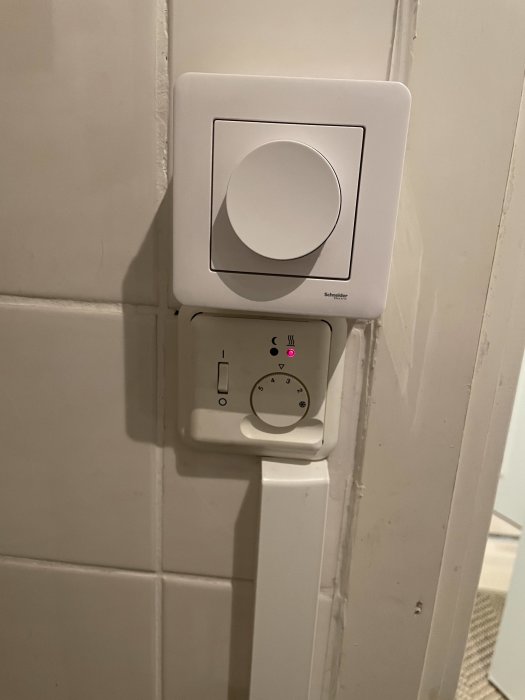 Nyinstallerad dimmer-ratt på vit vägg med kakel ovanför en strömbrytare och ett gammalt borrhål synligt.