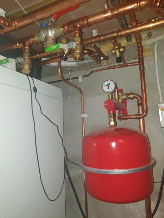 Installation med röda och kopparfärgade rör samt en röd expansionskärl i ett pannrum.