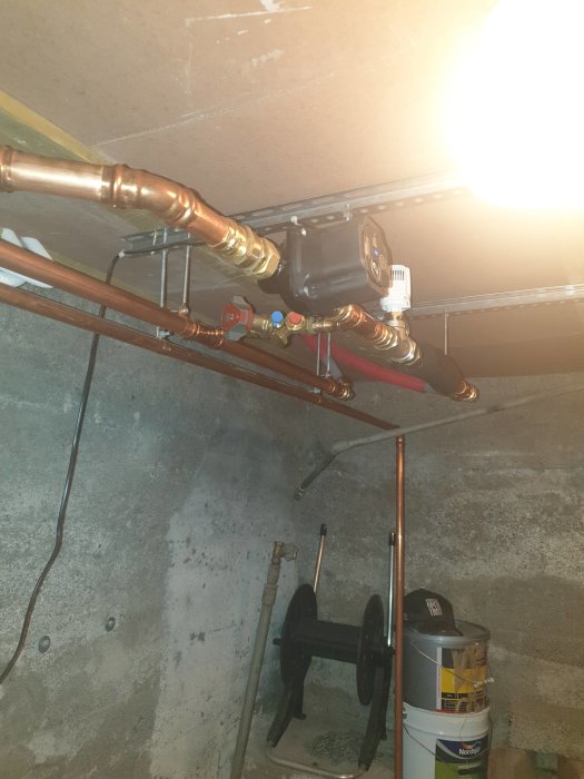 Kopparrör och värmeväxlare i ett grovt källarutrymme med synlig kabeldragning.