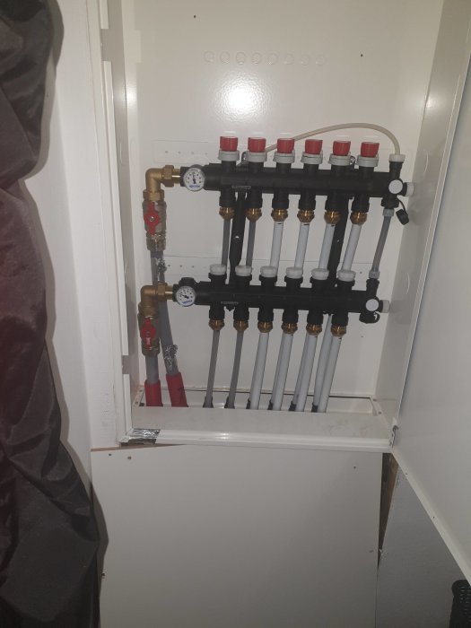 Installation av golvvärme med manifold, rör och avstängningsventiler i ett skåp.