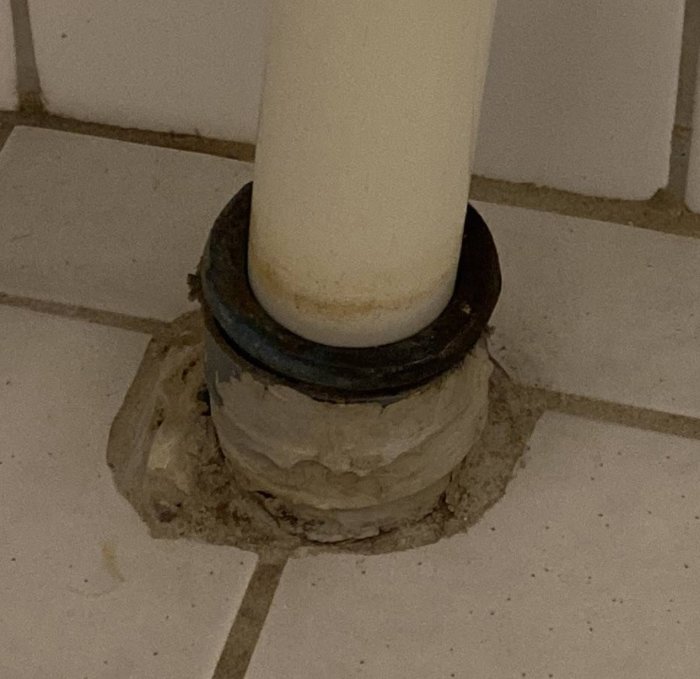 Äldre badrumsgolv med ett rör omgivet av tätskiktsguck och en manschett en bit upp på röret.