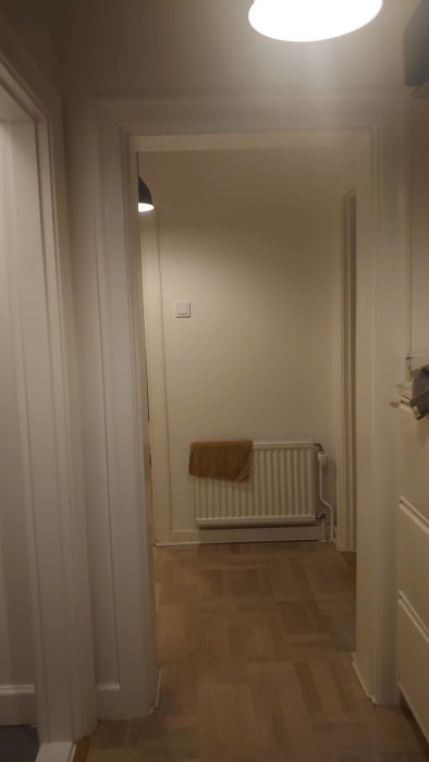 Hall med träradiator och parkettgolv, tänkt plats för ny luftpump till vänster om dörren.