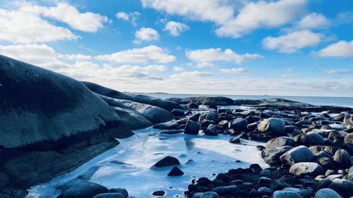 Vinterlandskap på Hönö med isbelagda klippor och stenar mot en klarblå himmel.