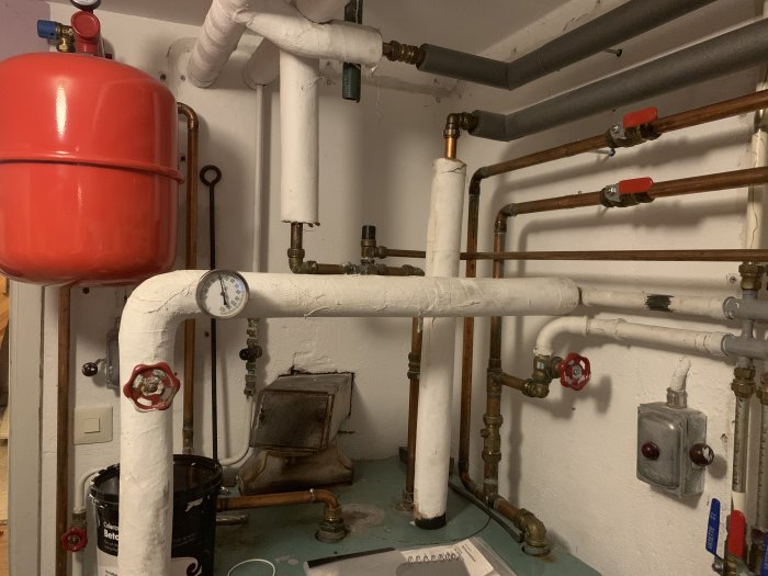 VVS-installation med rör, röd expansionskärl och tryckmätare i ett pannrum.