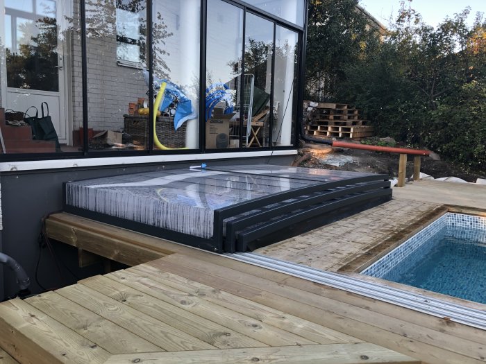 Pool med öppet mörkt taksystem Alva och omgivande trädäck under byggnation.