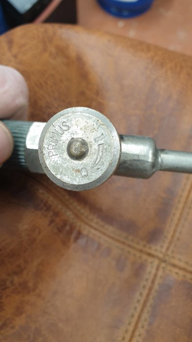 Gammal gasolbrännare med texten "PRIMUS" på munstycket, mot en bakgrund av brunt läder.