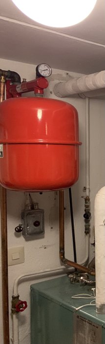 Expansionskärl och rörledningar i ett värmesystem med en röd ratt och manometer, indikerande en fråga om vattenavtappning.