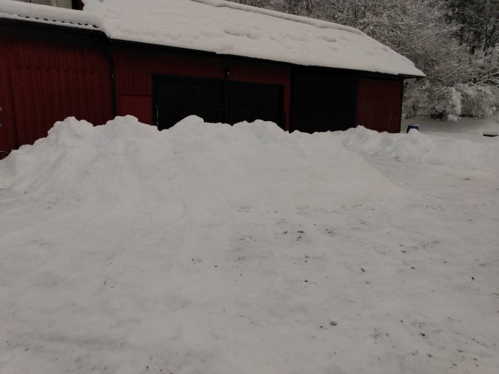 Snötäckt landskap med en stor snöhög framför en röd ladugård, tydliga tecken på vinter i Skåne.