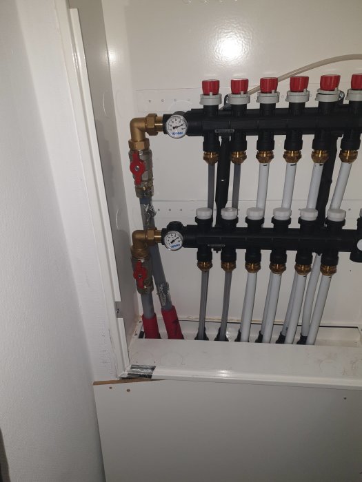 Värmesystemets fördelarskåp med rör och mätare visar värmen i returledningen.