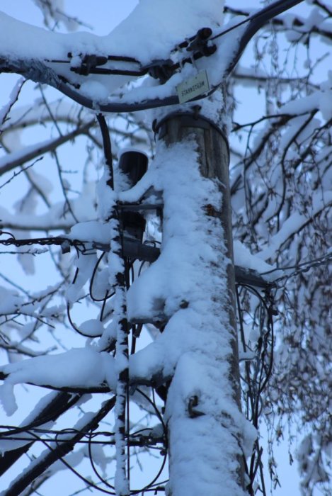 Elektrisk stolpe med luftledningar täckt av snö och skylt som anger 5-7 kW.