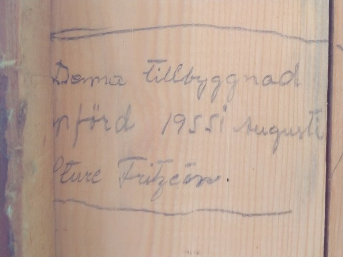 Handstil på träplank med texten "Denna tillbyggnad utförd 1955 i augusti av Sture Frigson" som dokumentation av renovering.