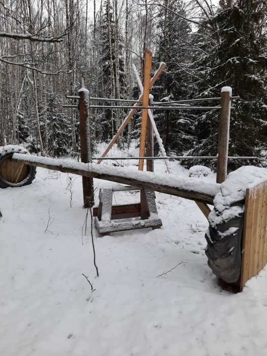 En gungbräda konstruerad av trä med rör i ett snötäckt landskap, stödd av trästolpar, med en krysslaser placerad på en stolpe.