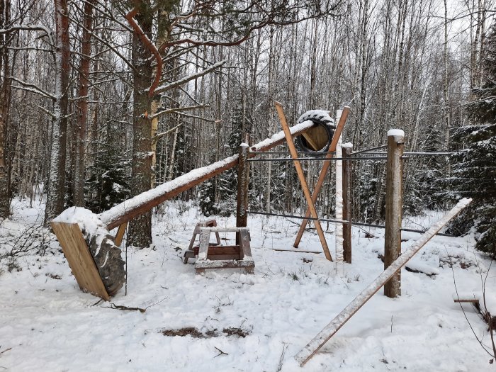 Gungbräda i skog med snö, konstruerad av trästockar och lyft av en traktordäck-vikt.