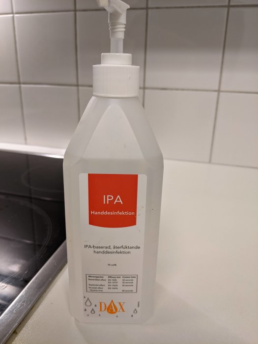 Flaska med IPA-baserad handdesinfektion märkt DAX på ett köksbänk mot kakelvägg.