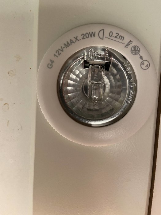 Närbild på en inbyggd G4 12V halogenlampa under ett skåp, med tekniska specifikationer tryckta runt armaturen.