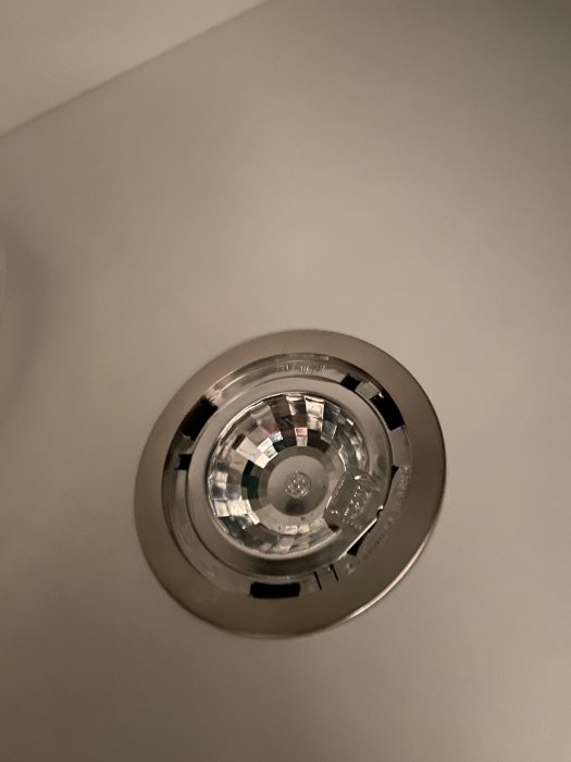Närbild på en inbyggd halogenlamparmatur i taket, med fokus på glödlampan och reflektor.