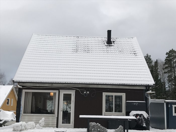 Ett hus med snötäckt tak där snön har smält vid skorstenen, indikerande möjlig värmeutstrålning.