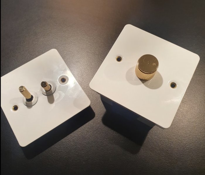 Två vita apparatdosor på en bordsskiva, en med utstickande anslutningar och en med guldfärgad ratt på toppen.