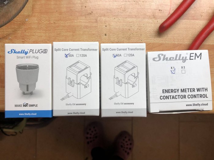 Fyra förpackningar av Shelly smarta elprodukter på ett golv, inklusive wifi-kontakt och energimätare.