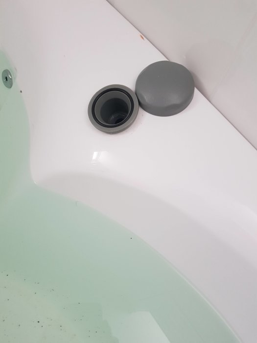 Närkort av ett hörn i ett spabad med vatten och en grå plastpåfyllningsöppning.