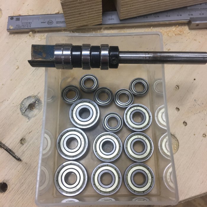 Ett verktygsskaft med dubbla lager ovanför en låda med flera nya kullager på ett arbetsbord.