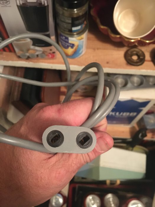 Hand håller en grå plastadapter med dubbla hål, troligtvis från en Nilfisk dammsugare.