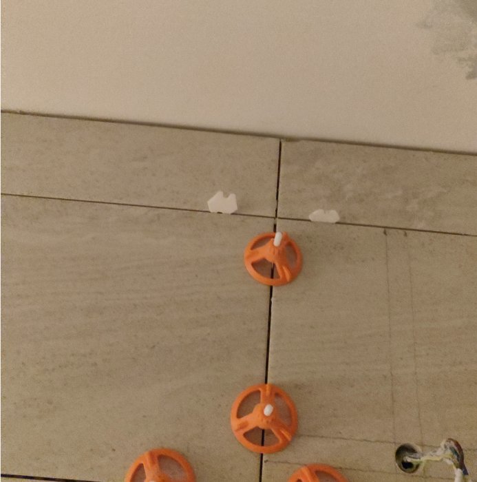 Flisad kakelplatta på vägg nära taket med orange kryssdistanser för kakelsättning.