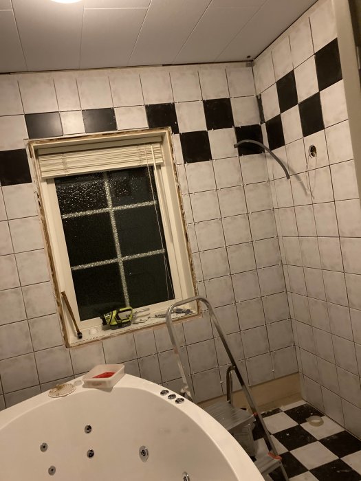 Kaklade väggar i svart och vitt runt ett fönster i ett badrum under renovering, med en stege och bubbelpool.