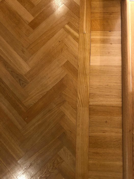 Fiskbensmönstrad parkettgolv bredvid ett trätröskel från en lägenhet byggd på 50-talet.