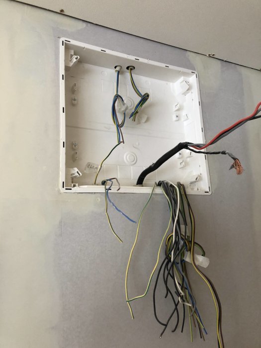 Öppen eldosa med lösa elektriska kablar på en vägg.