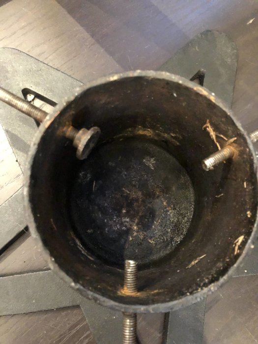 Närbild av en julgransfot med saknade stopp på skruvar, inuti stammen syns barrrester.