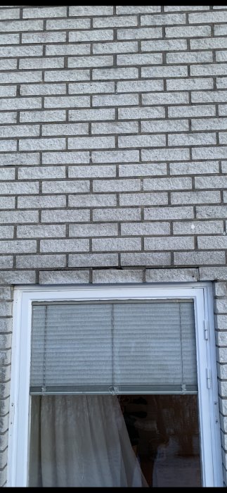 Mexi tegelvägg med skadad del ovanför vitramat fönster i behov av reparation.