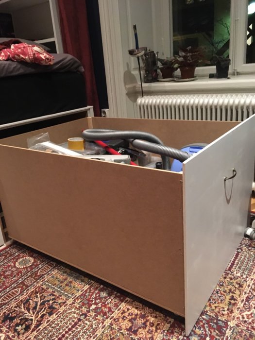 Hemmagjord förvaringslåda i plywood med handtag och innehåll av verktyg och sladdar.