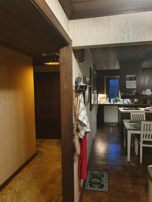 Interiör av ett timmerhus med synlig innervägg, dörröppning och kök i bakgrunden.