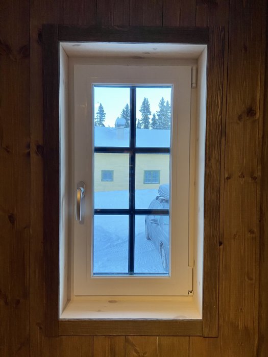 Nyligen installerat fönster med smyg och foder i ett rum med trätak och väggar, utsikt över snöigt landskap.