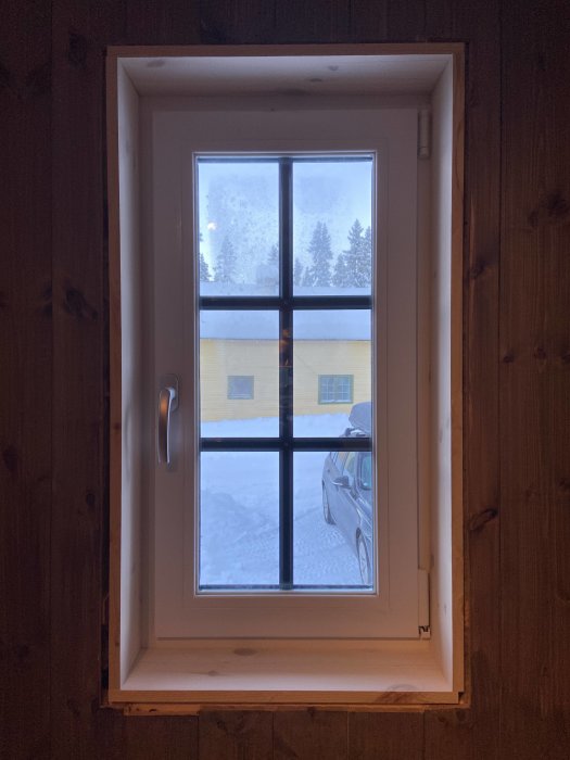 Nyligen installerat fönster med smygar och ofärdiga foder, utsikt över snö och gult hus.