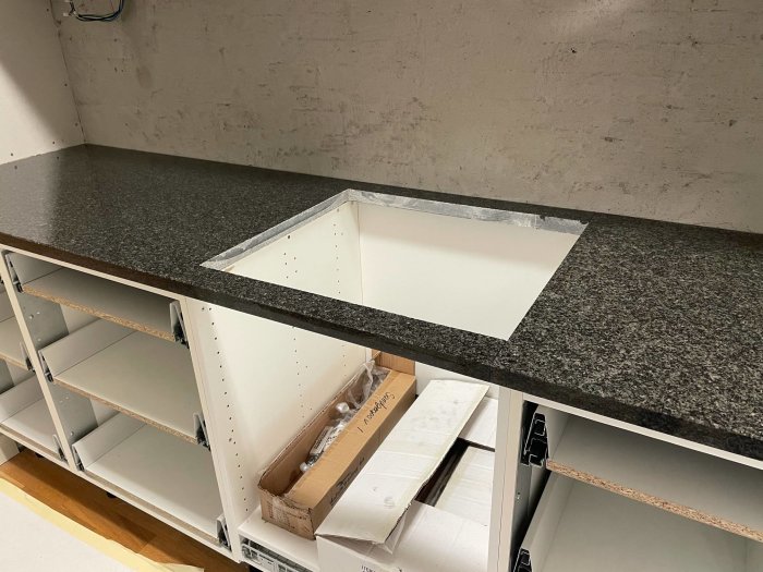 Bänkskiva i granit med synliga färgnyansskillnader, monterad på vita skåpstommar under konstruktion.