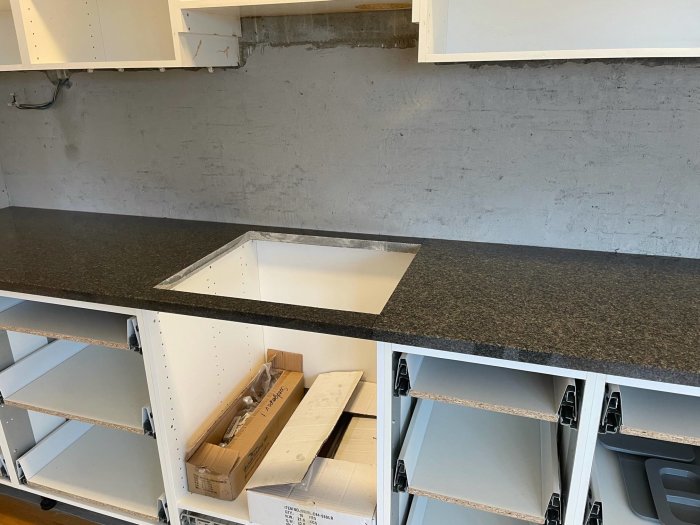 Granitbänkskiva i kök med synlig färgnuansskillnad mellan skivor, utsnitt för ho och öppna skåp undertill.