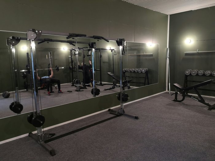 Ombyggt gym i ett tidigare hönshus med militärgröna väggar, stora speglar, styrketräningsmaskiner och viktskivor.