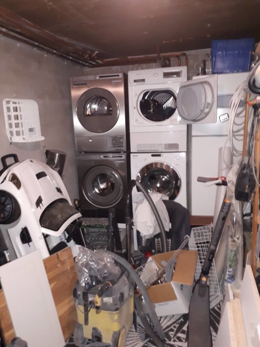 Rörigt tvättstuga med oorganiserade föremål framför tvättmaskin och torktumlare.