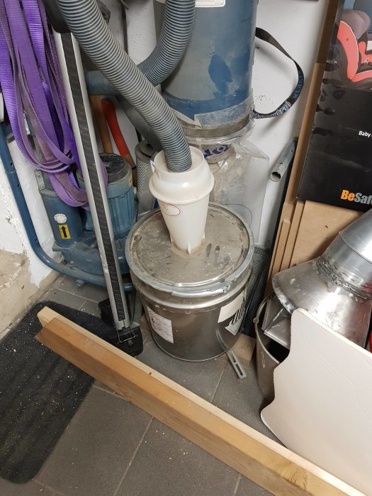 Arbetsrum med träplanka på golvet, spåntunna fylld med sågspån och olika verktyg.