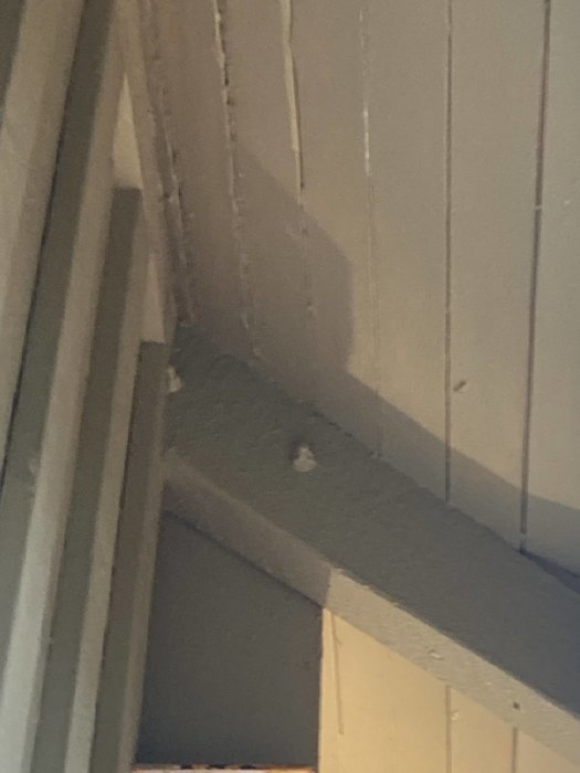 Skruv som delvis sitter fast i träbjälke med synlig tråd och skallig yta.